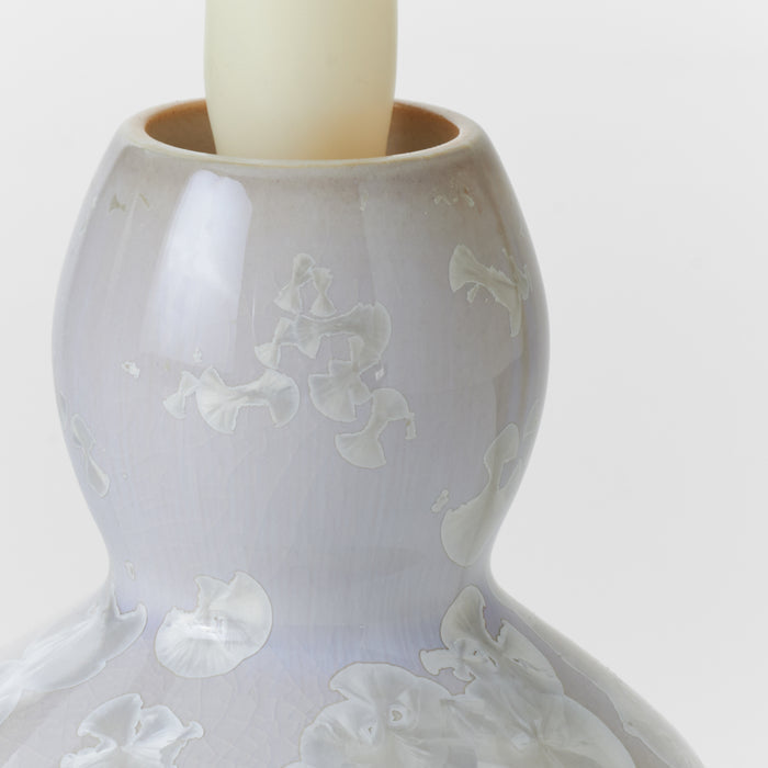 Cream-colored pottery candlestick with relief-molded floral motifs and ivory taper candle inserted in top socket.