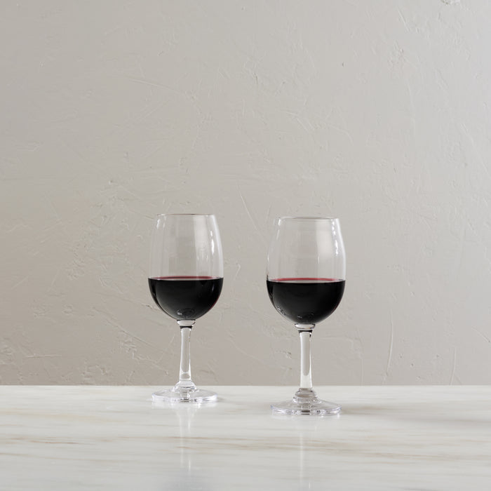 Two glasses filled with red wine on a white surface against a light textured wall.