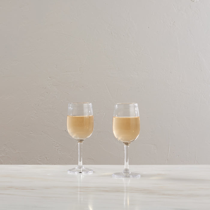 Two wine glasses filled with pale yellow wine on a white surface against a beige textured wall.