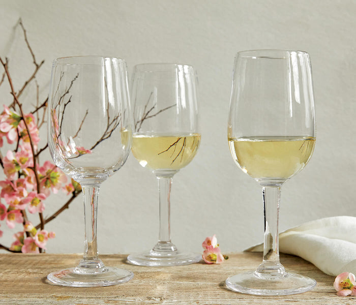 Two wine glasses filled with white wine and one empty glass displayed with pink flowers and a white cloth on a wooden surface